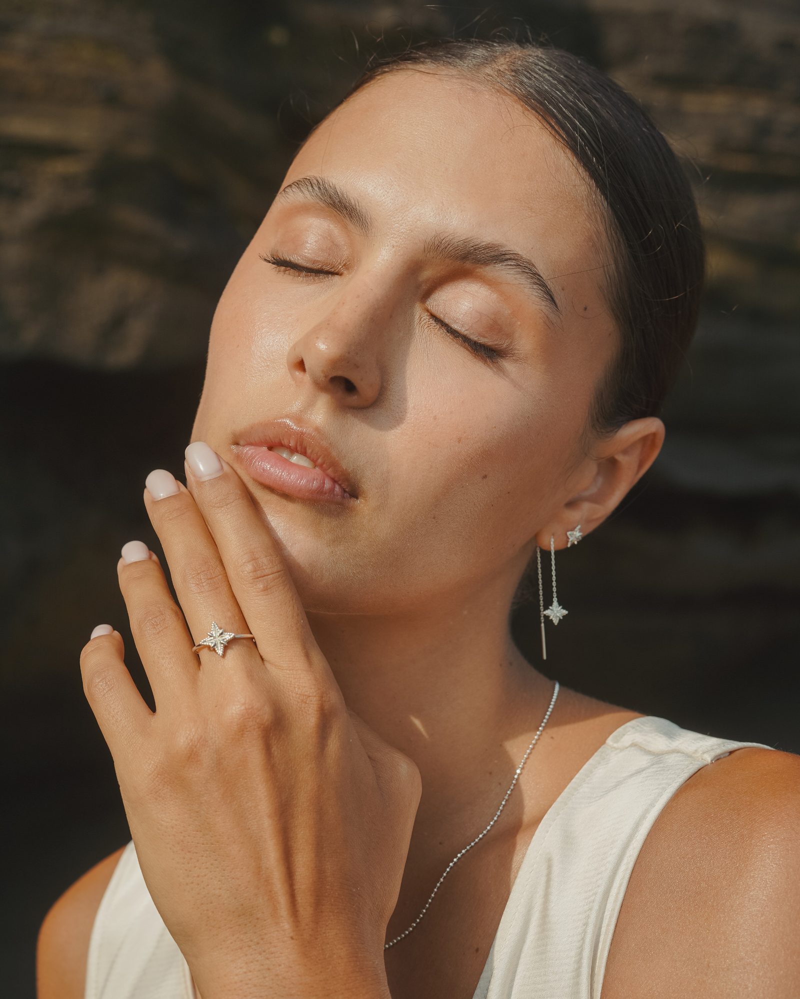 Frau mit geschlossenen Augen im Sonnenlicht, an der Hand ein Ring mit Stern, am Ohr ein Ohrring mit Stern