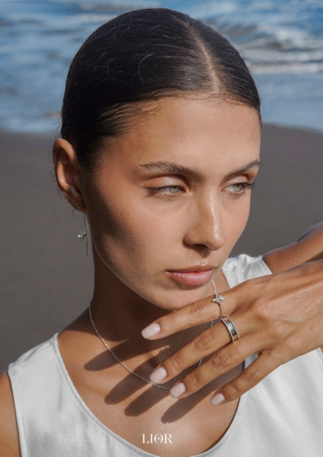 LIOR: Porträt einer Frau am Meer, die Hand mit Ringen am Gesicht